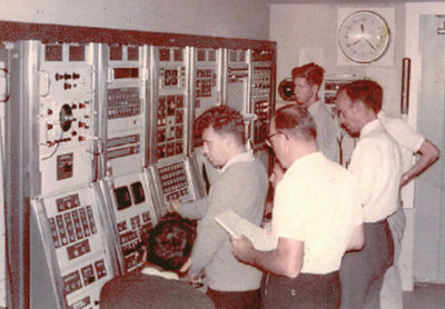 FPQ-6 Control console. Standing in the foreground is Ron Burgess with Geoge Allan in front of him operating the controls, then to the right Len Algate, Q6 Engineer; hidden behind him is Monte Sala, and at the back Mike Marsh. Seated are unknown RCA engineers? : Photo – George Allan